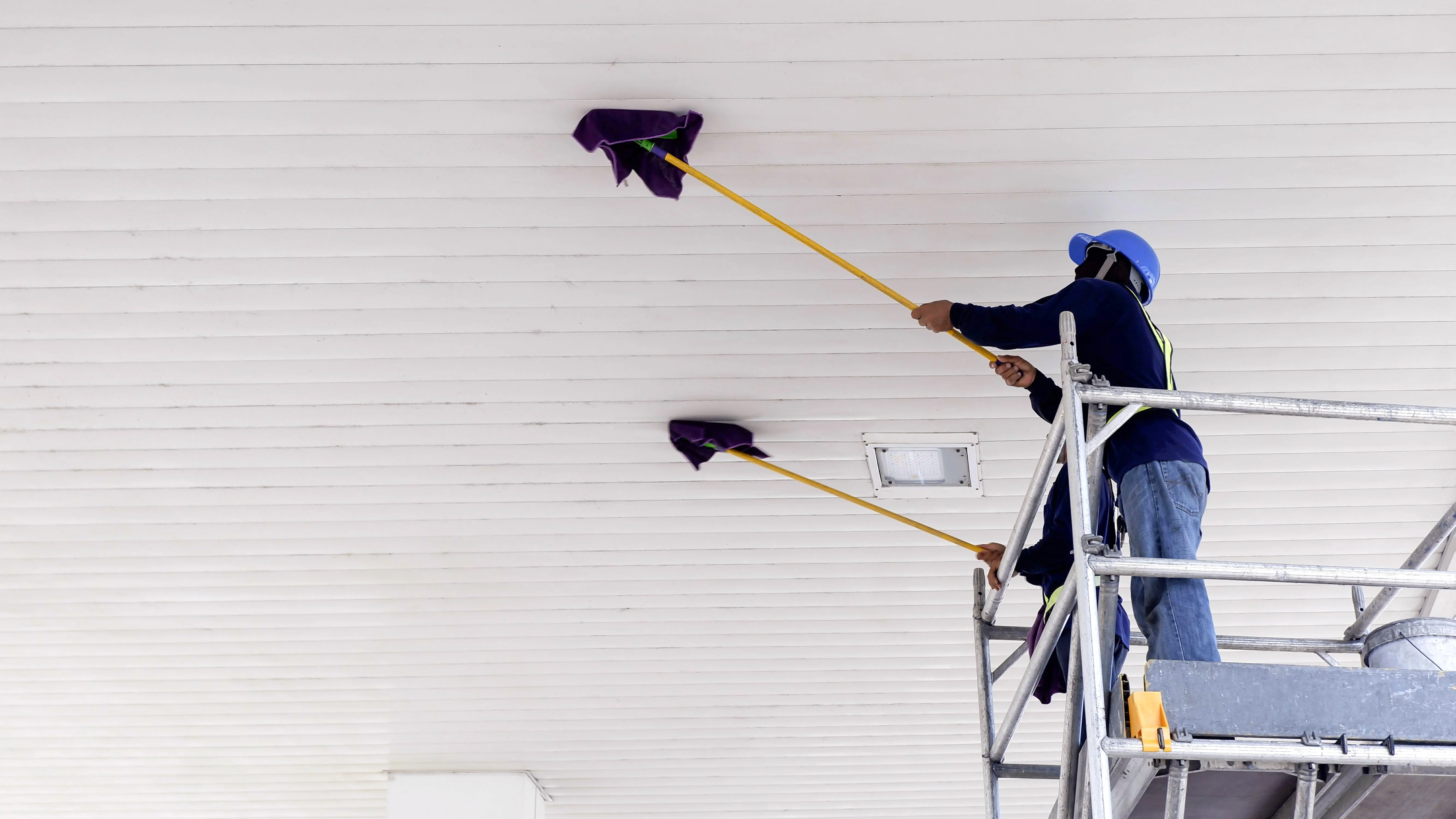 Professional cleaner removing construction dust from a ceiling during post construction cleaning